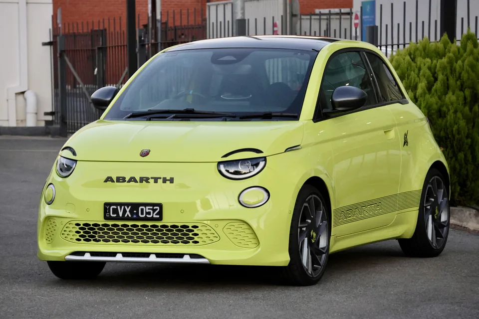 Yellow-green Abarth 500e, front three-quarter view, outdoor parking area