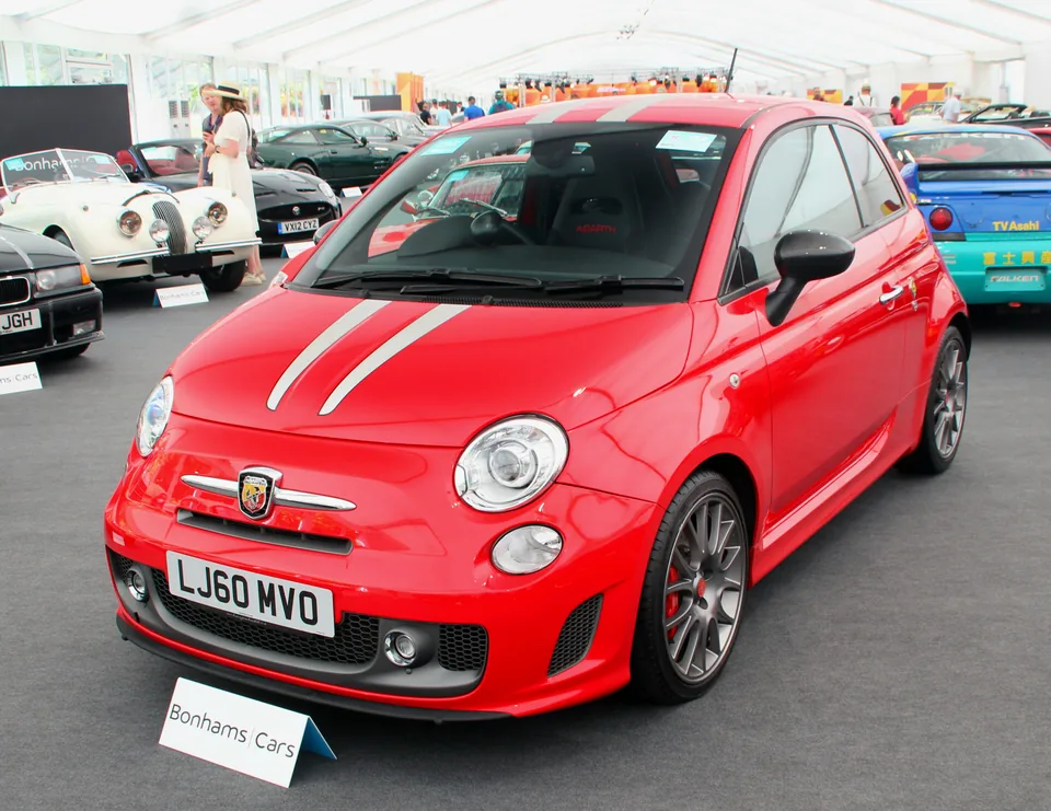 Red Abarth 695 Tributo Ferrari with white racing stripes, front three-quarter view, indoor car show