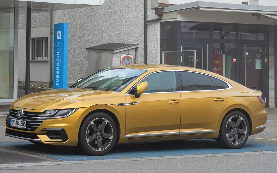 Kurkuma Yellow Volkswagen Arteon R-Line parked on a Swiss street, three-quarter front view