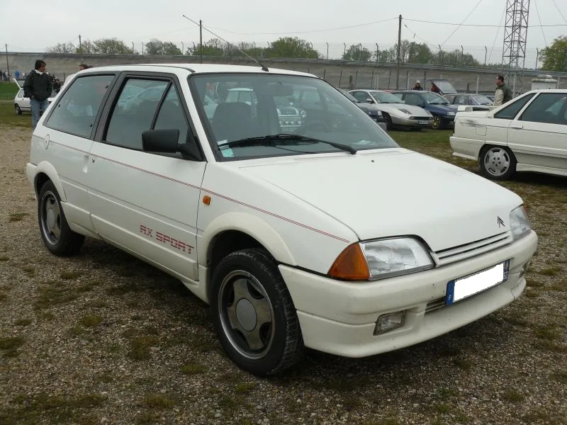 White Citroën AX Sport at a French circuit meeting, three-quarter front view with the AX SPORT door decal and white steel wheels