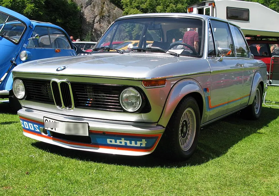 Silver BMW 2002 Turbo with factory Motorsport livery, front three-quarter view, car show on grass