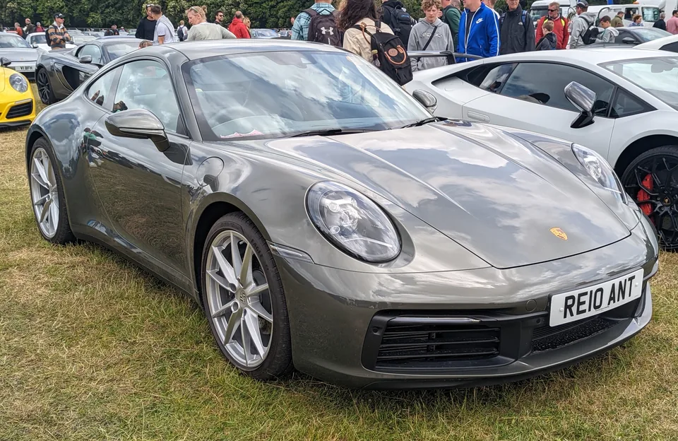Aventurine Green Metallic 2021 Porsche 911 Carrera (992) coupé with black brake calipers on grass at the Goodwood Festival of Speed, three-quarter front view