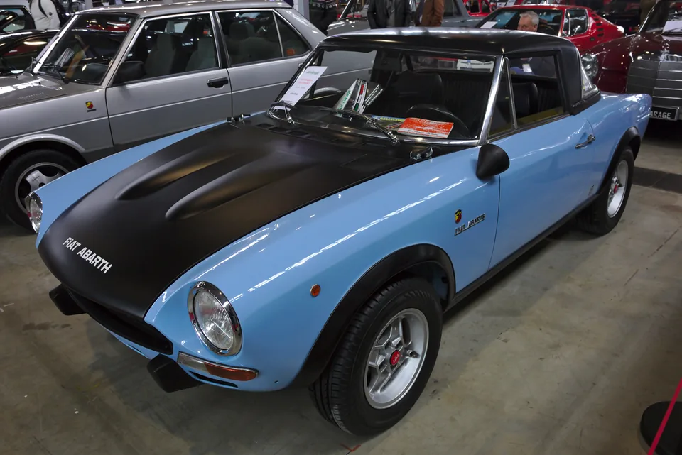 Light blue Fiat 124 Abarth Rally with black bonnet, front three-quarter view, indoor car show