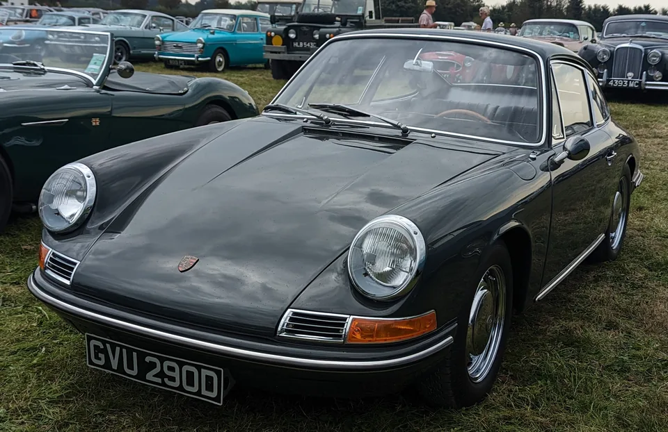 Slate grey 1966 Porsche 911 2.0 coupé on steel wheels with chrome hubcaps on grass at the Goodwood Revival, three-quarter front view