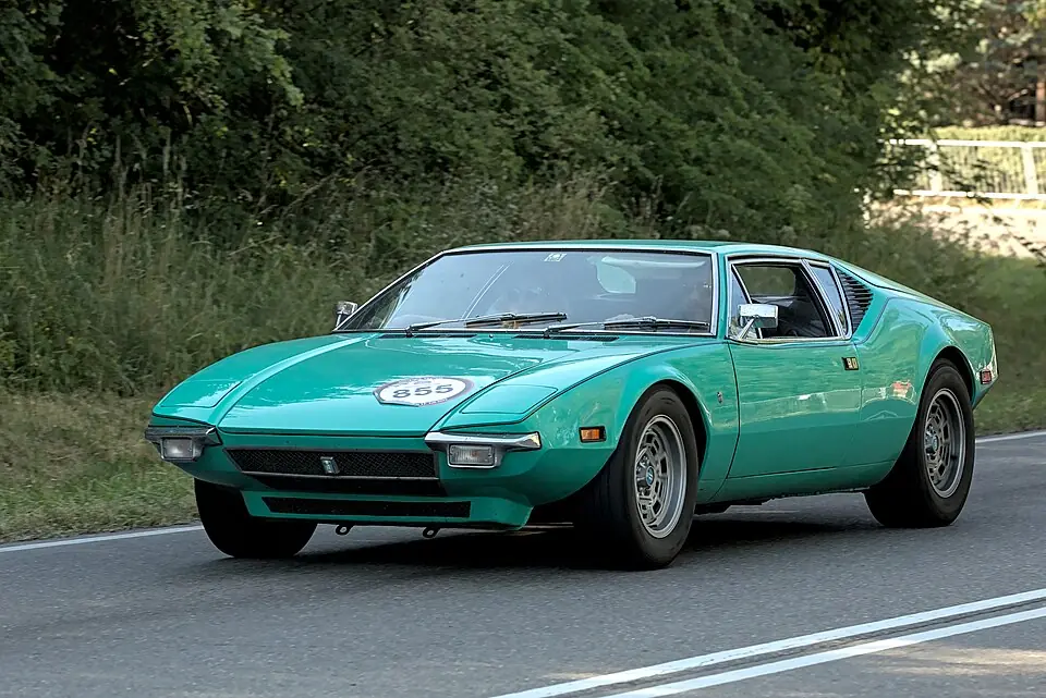 Teal green De Tomaso Pantera, front three-quarter view, driven on a tour road