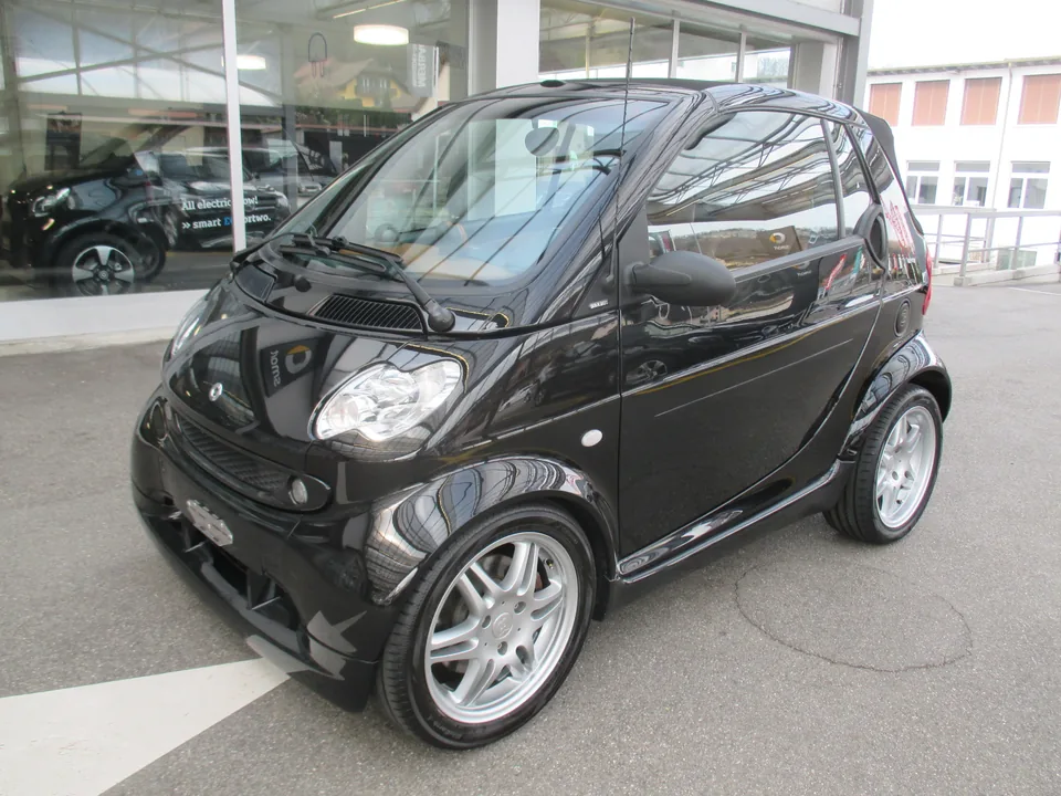 Black Smart Fortwo Brabus (450) cabriolet at a dealership, three-quarter front view with the BRABUS badge on the B-pillar